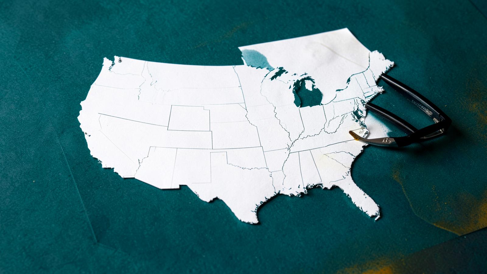 Printed map of the United States with reading glasses and a pen on a deep teal desk